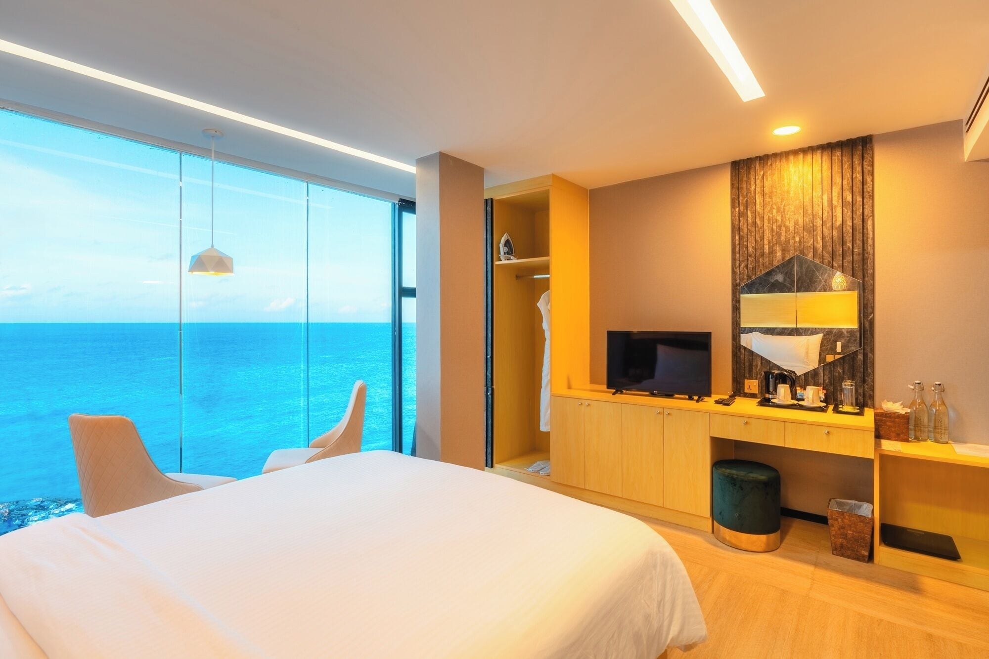 Un hotel moderno con una cama grande, televisión, espejo y vistas al océano.