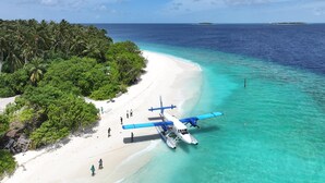 Un avión en la playa con agua turquesa cristalina y una isla boscosa al fondo.