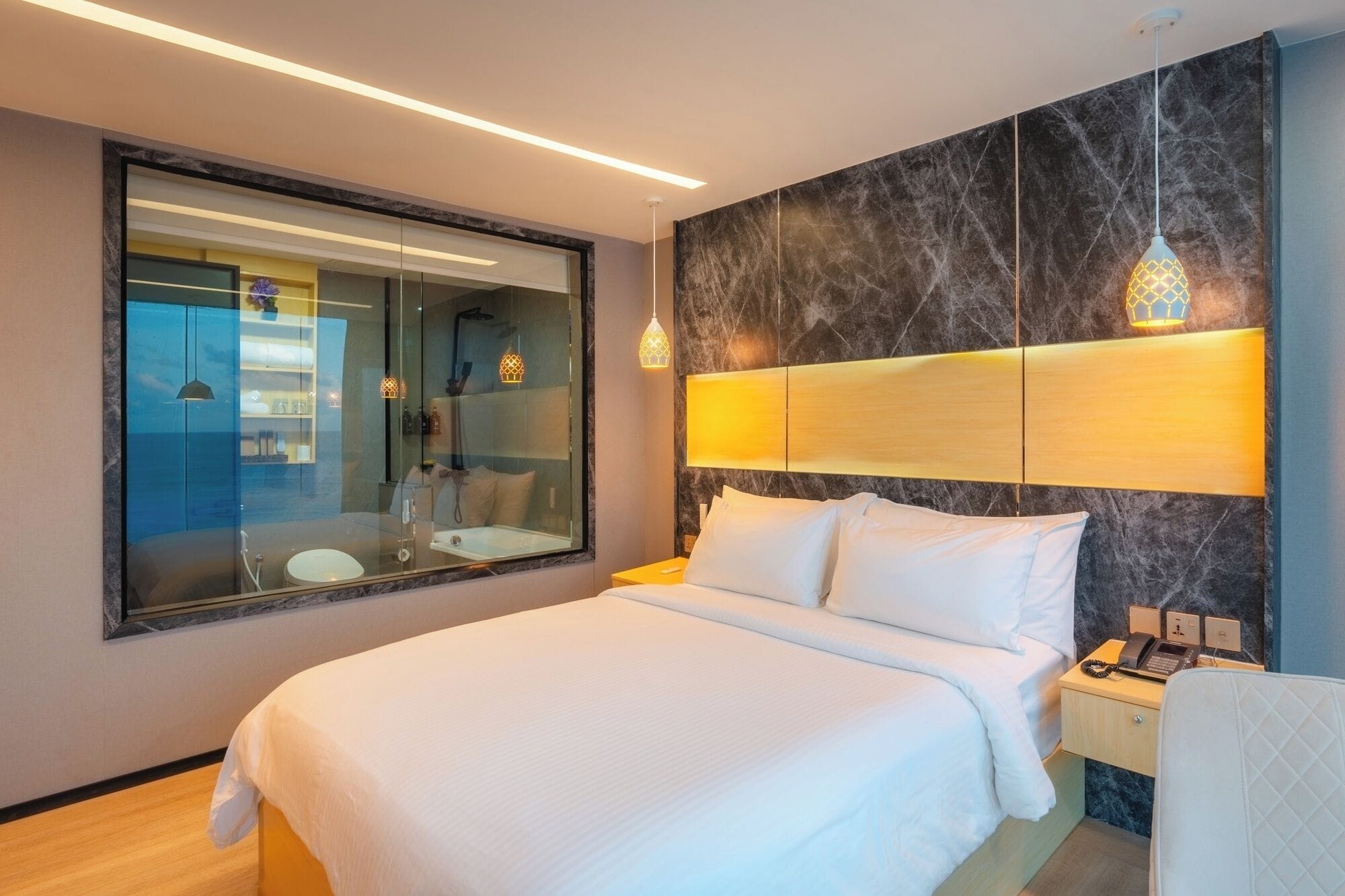 A modern hotel room with a large bed, a glass-enclosed bathroom, and a marble accent wall.