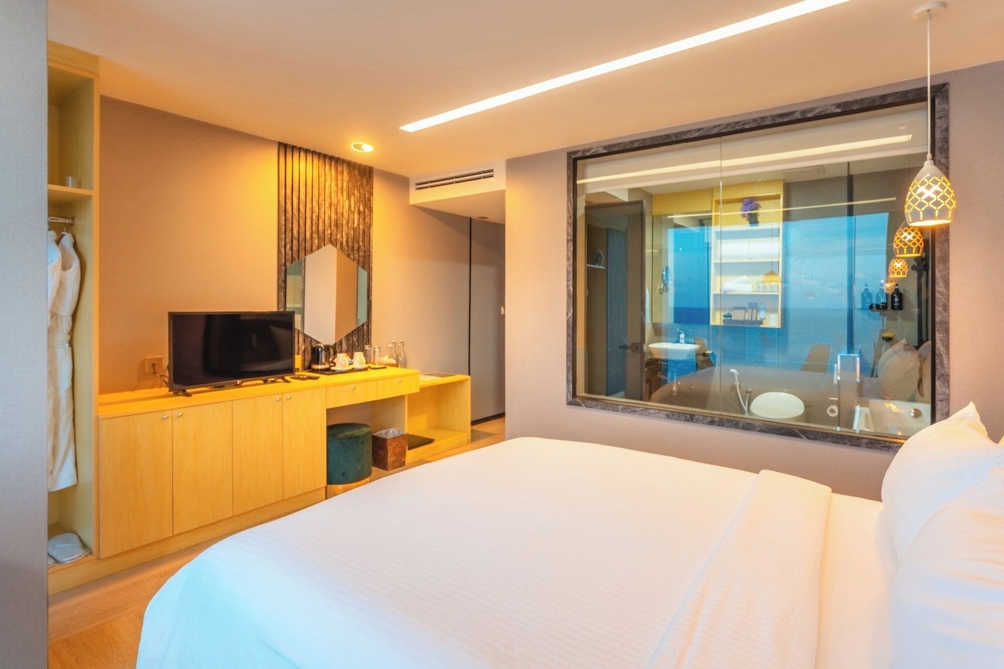 Habitación de hotel con cama, televisión, minibar y baño con un espejo grande, además de vista al mar.