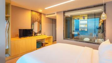 Habitación de hotel con cama, televisión, minibar y baño con un espejo grande, además de vista al mar.