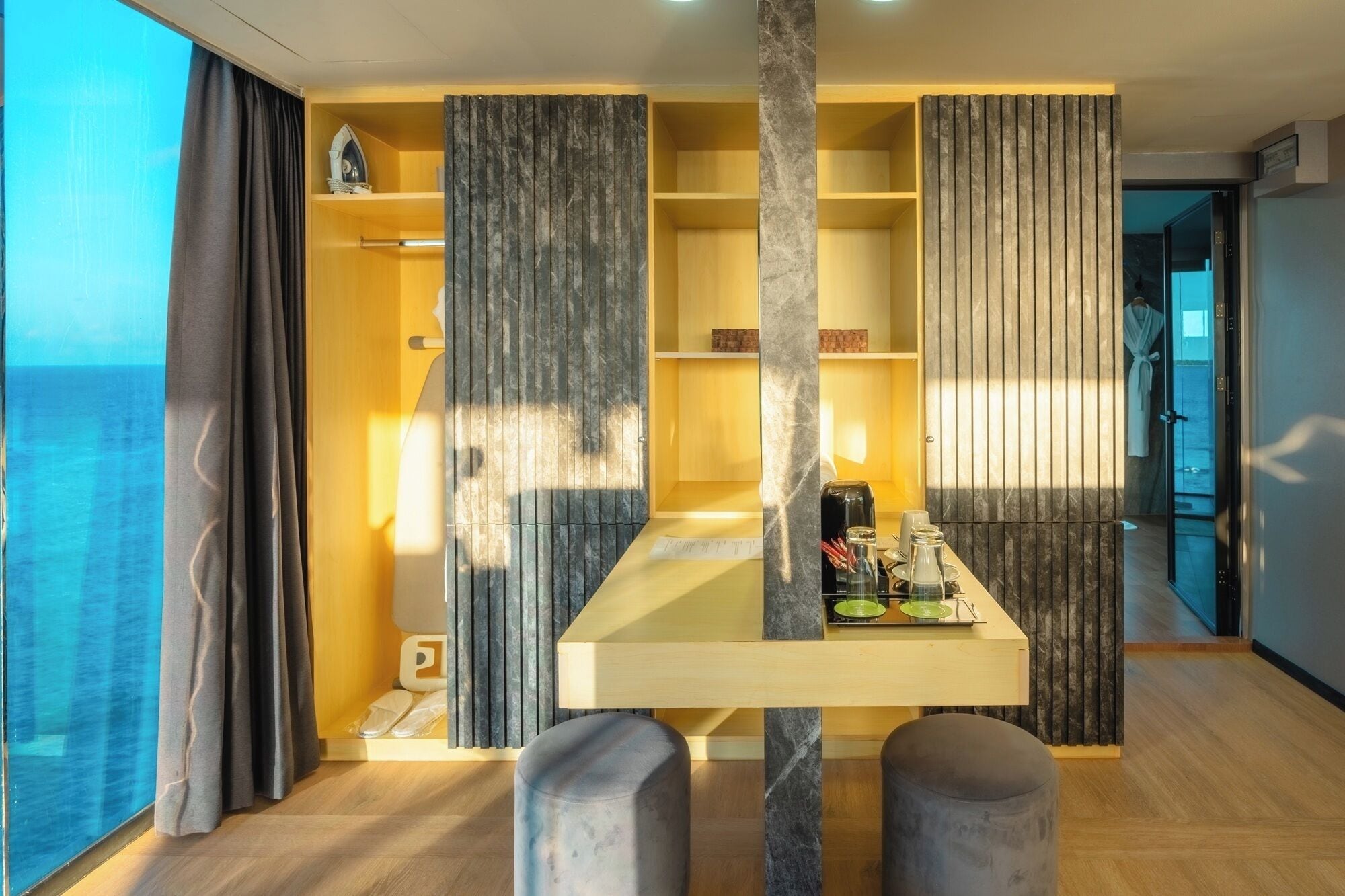 A modern room with a wooden table, two grey ottomans, and a view of the sea.