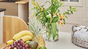 Une cuisine avec un mur en briques, un meuble blanc aux portes vitrées et un panier de fruits posé sur le plan de travail.