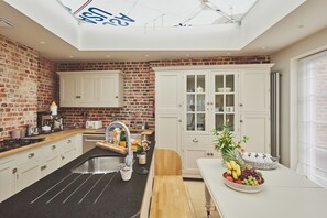 Een keuken met een bakstenen muur, witte kastjes, een houten aanrecht en een dakraam.