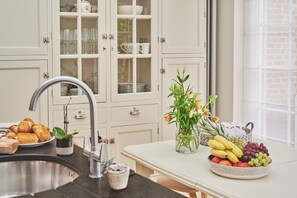 Een keuken met een spoelbak, een aanrecht met een fruitschaal, en een kast met glazen deuren met servies.