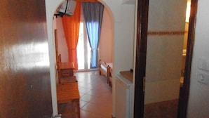 A hallway with a wooden chair, a small table, and a bed in the background. - Julieta's House (Alonissos)