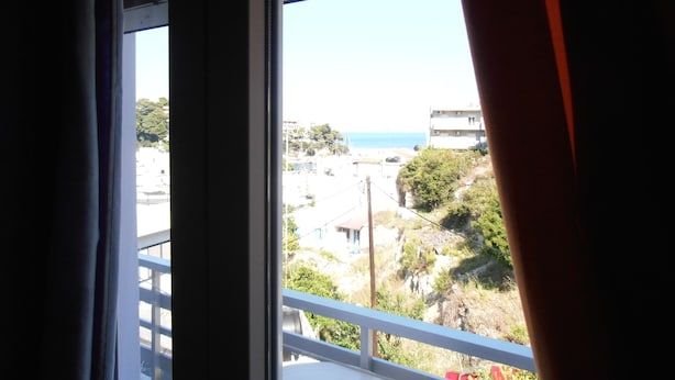 A view through a window with a balcony, overlooking a beach and buildings. - Julieta's House (Alonissos)