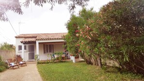 Une maison avec un toit en tuiles, une cour clôturée et un petit jardin agrémenté d’une table et de chaises.