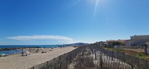A beach with a wooden fence, beachgoers, and houses in the background. - Beach house 30 meters from the sea for 5/6 people (Blue Flag beach) (Frontignan plage)