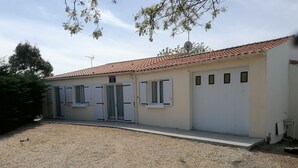 A building with a tiled roof, a gravel driveway, and a door with a sign above it. - Maison Bord de mer (Brem-sur-Mer)