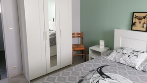 A bedroom with a bed, a wardrobe, a chair, a bedside table, and a wall with a framed picture. - Maison Bord de mer (Brem-sur-Mer)
