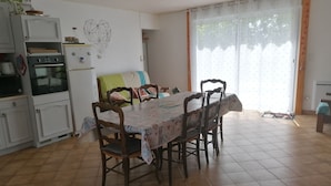 A dining area with a table and chairs, a kitchen with appliances, and a sliding glass door to the outside. - Maison Bord de mer (Brem-sur-Mer)
