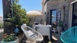 Una terraza de madera con mobiliario exterior, incluyendo una silla lounge blanca, una silla turquesa y una mesa con una piña como centro de mesa.