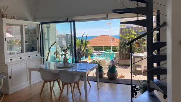 Una cocina moderna con zona de comedor, ventanas amplias y vista a una piscina y el océano.