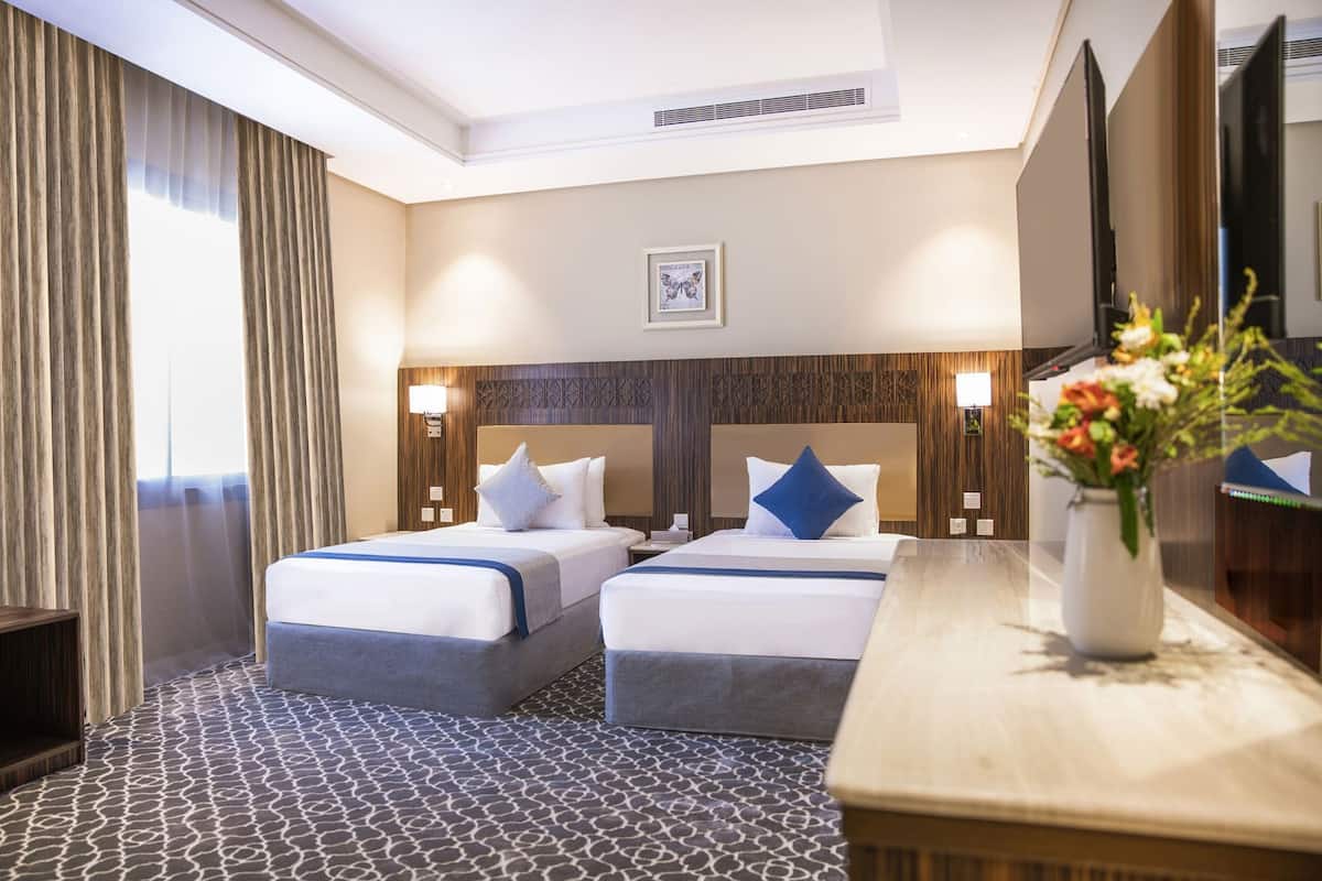 A hotel room with two beds, a wooden headboard, a patterned carpet, a vase with flowers, and a mirror.