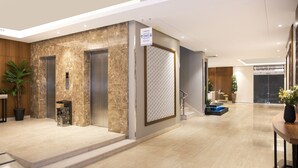 Un vestíbulo moderno con suelo de mármol, dos ascensores, una escalera y un mostrador de recepción.