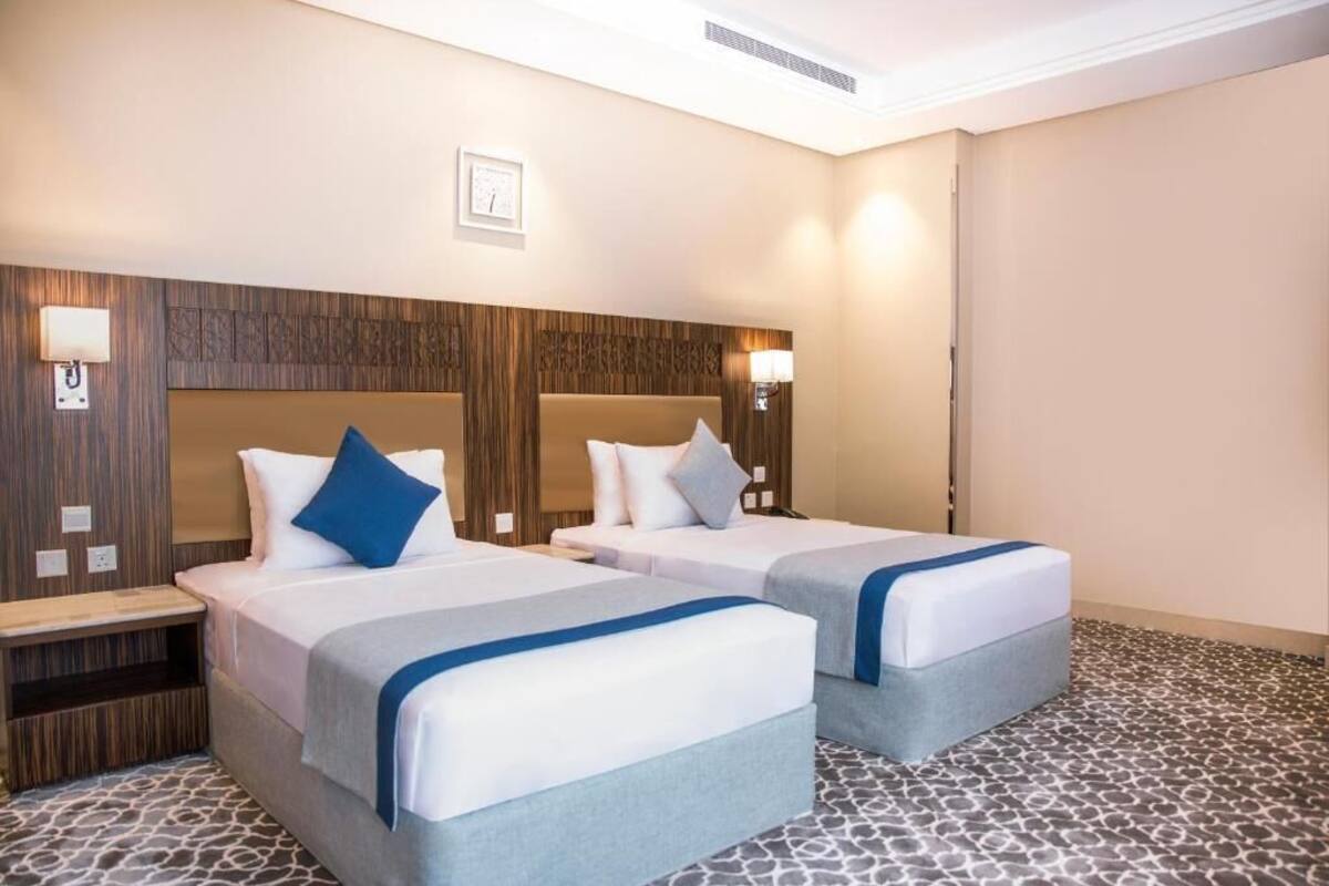 A hotel room with two beds, a wooden headboard, bedside lamps, and a patterned floor.