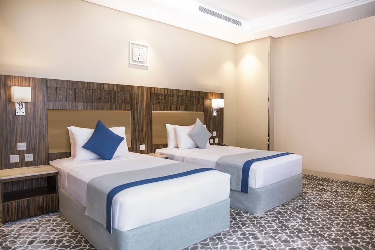 A hotel room with two beds, a wooden headboard, bedside lamps, and a patterned floor.