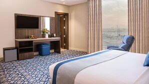 Habitación de hotel con cama, escritorio, televisor de pantalla plana, silla y ventana grande con vistas a la ciudad.