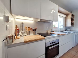 Una cocina moderna con armarios blancos, horno empotrado, campana extractora de acero inoxidable y encimera de madera.