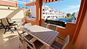 Un balcón con una mesa y sillas, un televisor y vistas a una piscina y edificios.