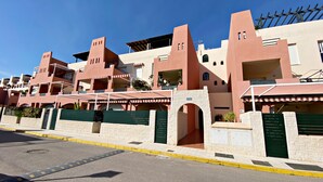 Una hilera de edificios modernos con balcones, un acceso con portón y un cielo despejado.