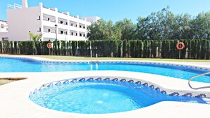 Una piscina con borde de azulejos, un puesto de salvavidas y un edificio al fondo.