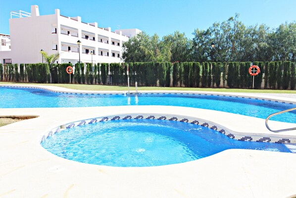 A swimming pool with a tiled edge, a lifeguard stand, and a building in the background.
