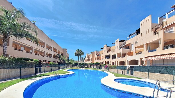A swimming pool with a curved design, surrounded by multi-story buildings with balconies and a clear sky. - Nassau - Apartment with terrace and pool in Vera Playa (Vera playa)