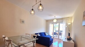 A modern living room with a glass dining table, white chairs, a blue sofa, and a small white side table. - Nassau - Apartment with terrace and pool in Vera Playa (Vera playa)