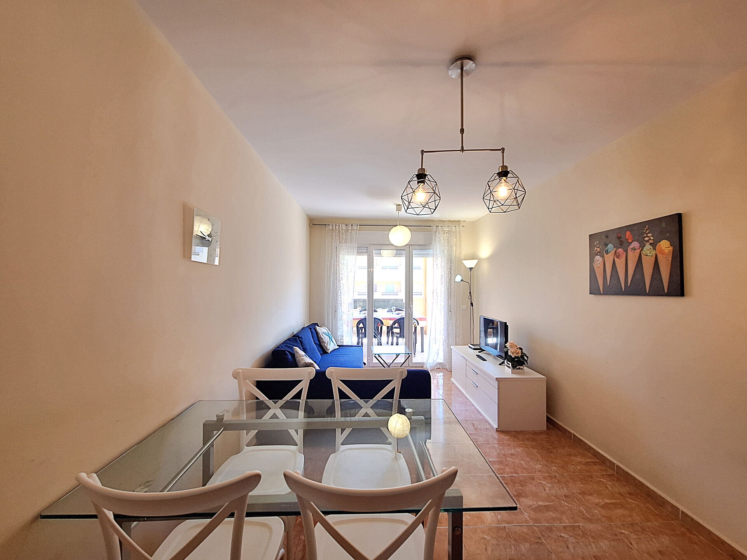 A dining area with a glass table and chairs, a sofa, a TV, and a painting on the wall.