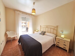 Un dormitorio con cama, mesitas de noche, una silla y una ventana con cortinas.