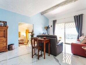 Una sala de estar con un sofá, una mesa de comedor con sillas, un aparador de madera y vistas a través de un ventanal grande.