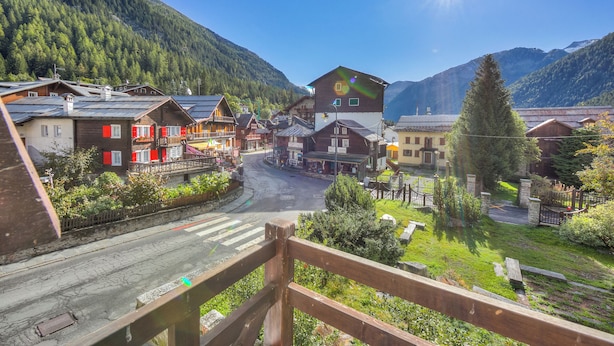 Ein Bergdorf mit traditionellen Holzhäusern, einer klaren Straße und Blick auf den umliegenden Wald und die Berge.