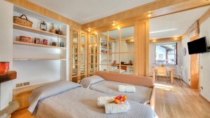 Ein Hotelzimmer mit zwei Betten, Holzregalen, einem Fernseher und einem kleinen Tisch.