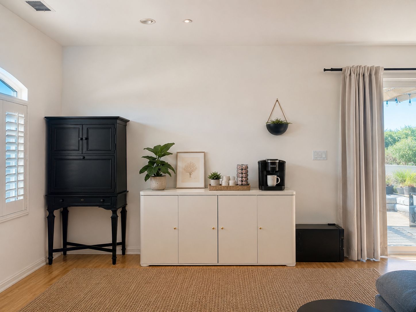 A room with a white cabinet, a black cabinet, a coffee maker, a framed picture, and a hanging plant.