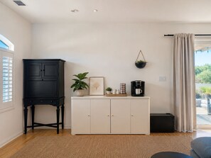 A room with a white cabinet, a black cabinet, a coffee maker, a framed picture, and a hanging plant.