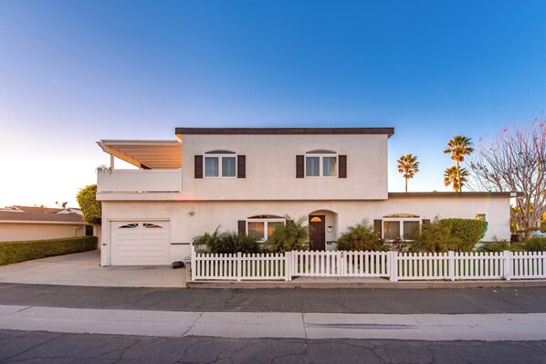 A two-story house with a white picket fence, a garage, and a small porch. - Luxury Beach House 99 Steps from Sand, Pet-friendly (Ventura)