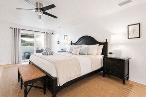 A bedroom with a bed, bedside tables, a bench, a ceiling fan, and a view through a sliding door. - Luxury Beach House 99 Steps from Sand, Pet-friendly (Ventura)
