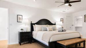Une chambre à coucher avec un lit, des tables de chevet, un banc et un ventilateur de plafond.