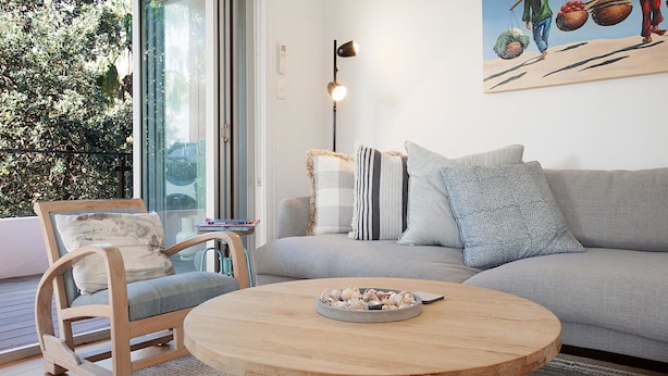 A modern living room with a grey sofa, a wooden coffee table, and a chair. There is a painting on the wall and a floor lamp.