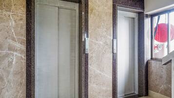 Two elevator doors with marble walls and a window with a red object outside.