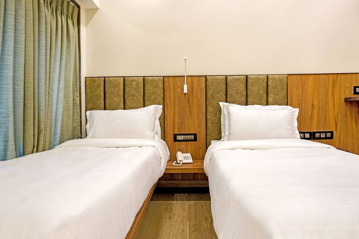 A hotel room with two beds, a wooden headboard, a bedside table with a phone, and a curtain.