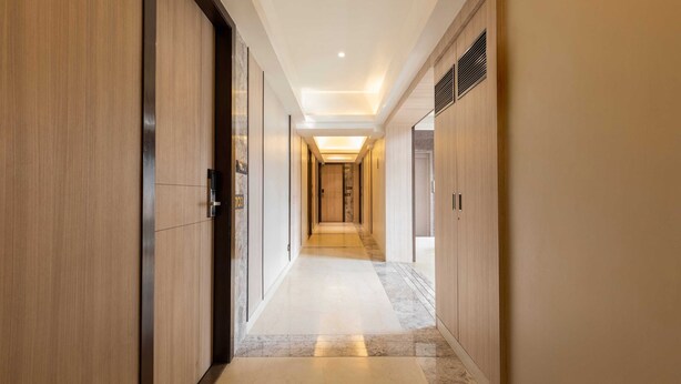 Un pasillo moderno de hotel con paneles de madera, suelo de mármol e iluminación empotrada.