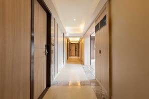 A modern hotel corridor with wooden paneling, a marble floor, and recessed lighting. - HOTEL OLTEN (Mumbai)