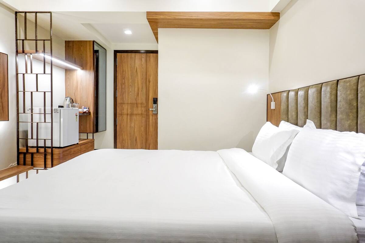 A hotel room with a large bed, wooden headboard, a small kitchenette, and a wooden partition.