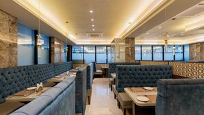 Un restaurante con cabinas de respaldo alto y mesas, piso de mármol y vistas a través de amplias ventanas.
