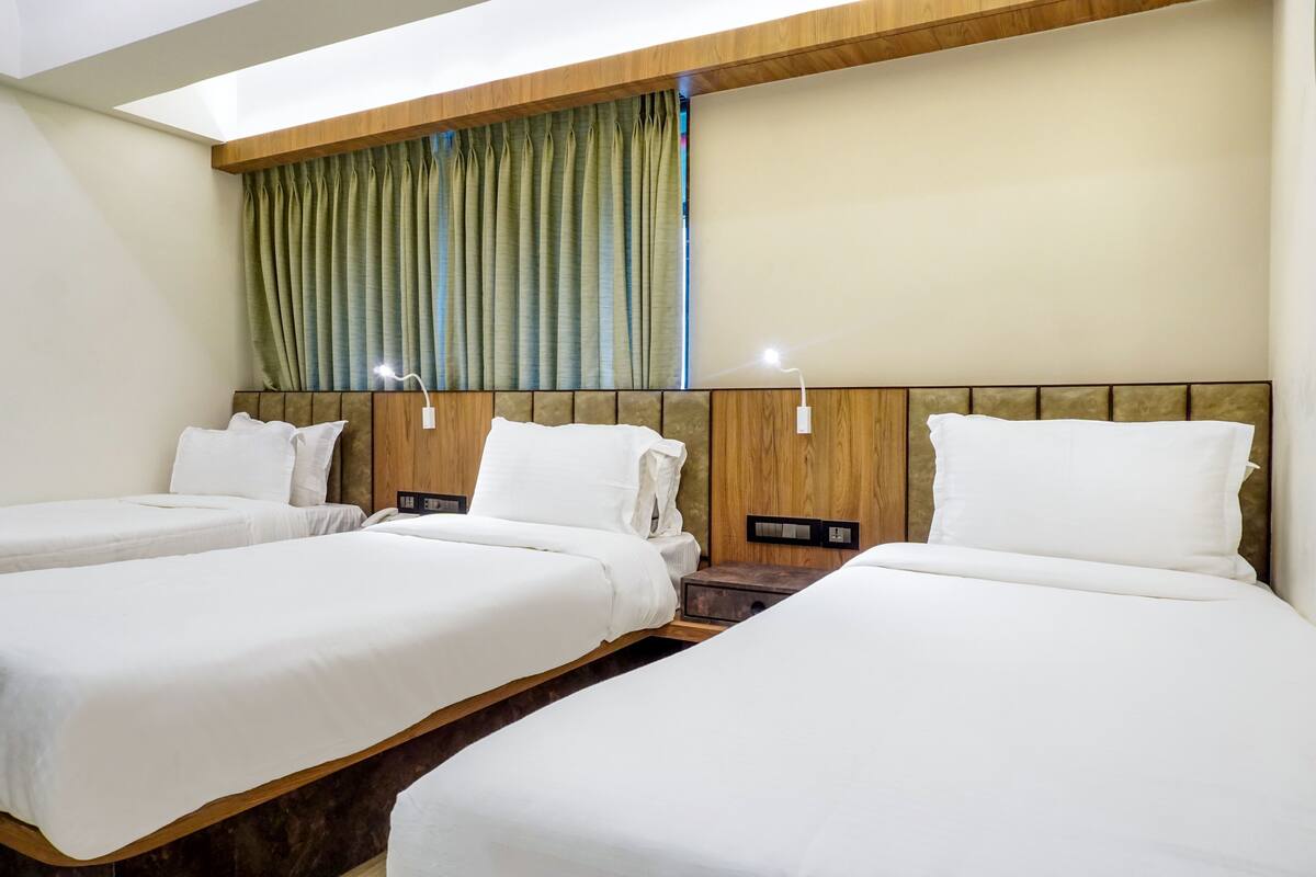 A hotel room with three beds, wooden headboards, and a window with curtains.