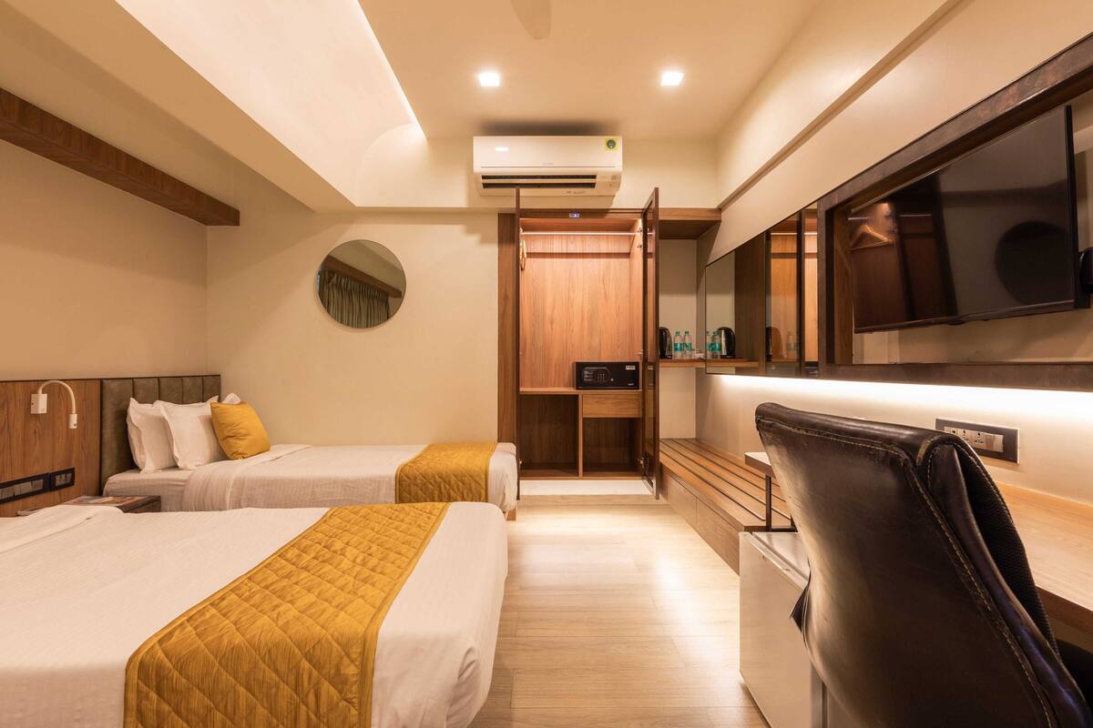 A hotel room with two beds, a desk, a mirror, and a television.