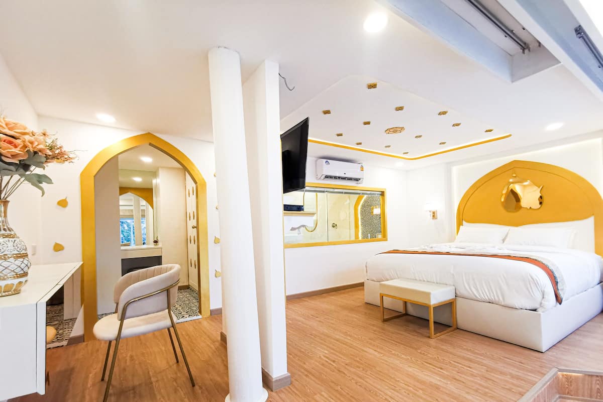 Une chambre d’hôtel moderne avec un plancher en bois, un lit doté d’une tête de lit blanche, un bureau avec une chaise et un grand miroir.